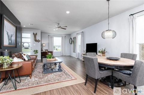 A modern living room with a brown leather sofa, a wooden coffee table, and a dining table set up with grey chairs.