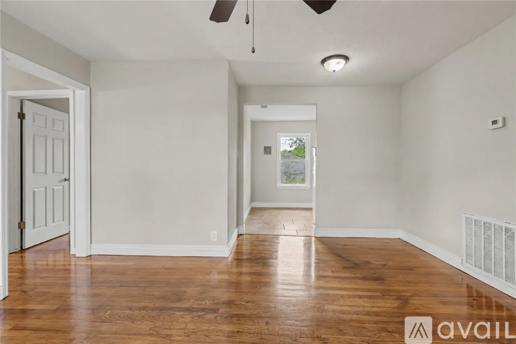 A room with wooden floors and white walls, a ceiling fan, and a window with a view of trees.