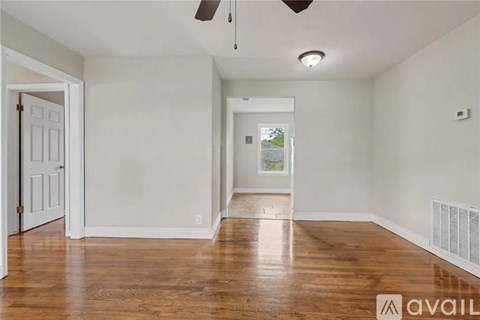 A room with wooden floors and white walls, a ceiling fan, and a window with a view of trees.