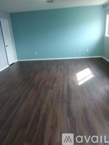 A room with wooden flooring and a door on the left side.