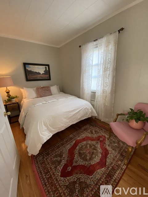 A bedroom with a large bed, a pink chair, and a rug with a red design.
