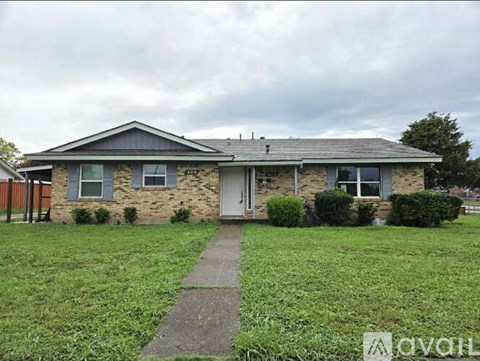 A house with a grey roof and a white door is surrounded by a grassy lawn.