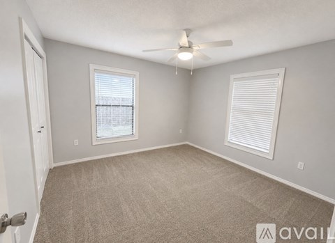 A room with a carpeted floor, a ceiling fan, and two windows with blinds.