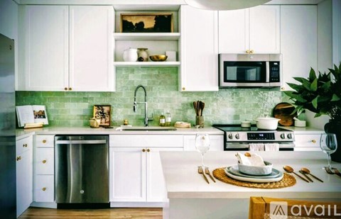 A kitchen with white cabinets and a green backsplash.
