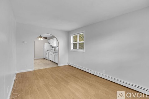 A room with wooden flooring and white walls, with a window on the right wall.