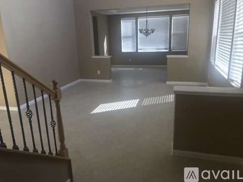 A room with a staircase on the left and a window with blinds on the right.