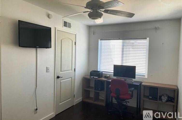 A room with a ceiling fan, a desk with a computer, and a door.