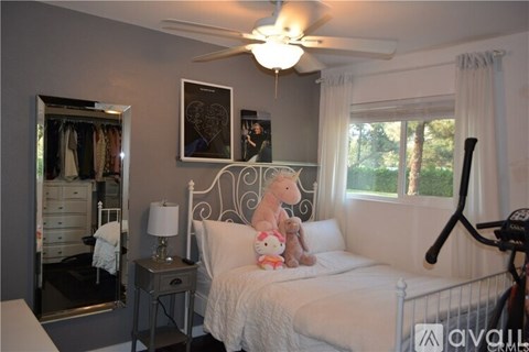A bedroom with a bed, a nightstand, a ceiling fan, and a window with white curtains.