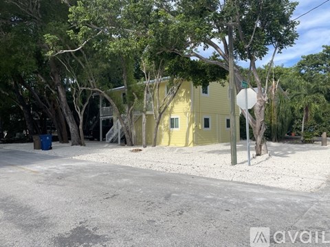 A yellow building is surrounded by trees and a street sign is in front of it.