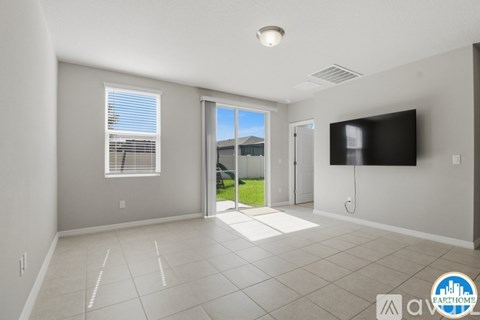 A spacious living room with a flat screen TV mounted on the wall and a sliding glass door leading to a balcony.