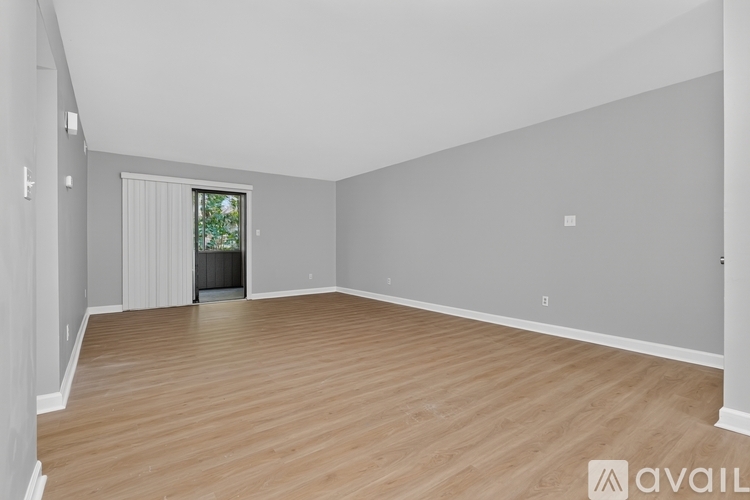 A spacious room with wooden flooring and a window with blinds.