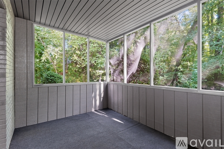 A room with a wooden ceiling and walls, large windows with a view of trees outside.