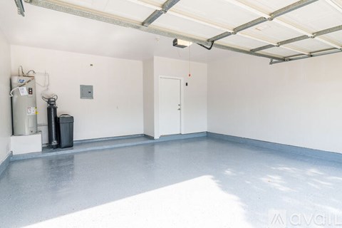 A spacious garage with a white floor and walls, equipped with a water heater and a trash can.