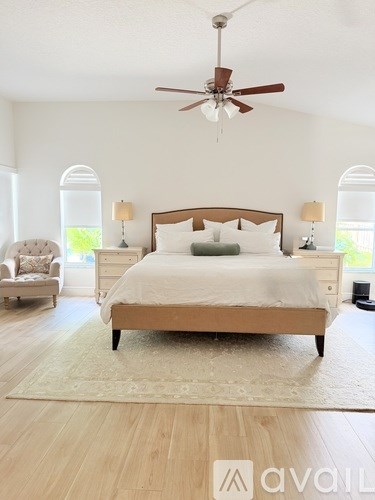 A bedroom with a large bed, a ceiling fan, and a chair.