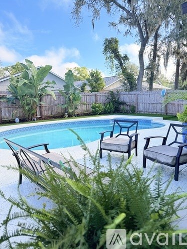 A pool with chairs and a fence in the background.