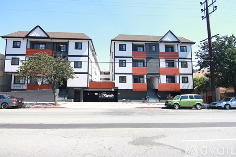 Two apartment buildings with cars parked in front.