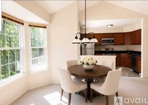 A dining room with a round table and chairs, a chandelier, and a kitchen in the background.