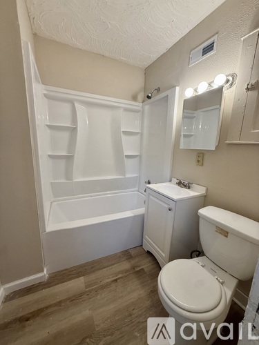 A white toilet sits in a bathroom with a white bathtub and a white cabinet.