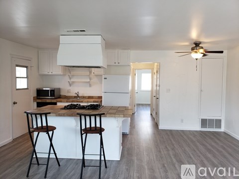 A kitchen with white cabinets and a wooden island with two chairs.