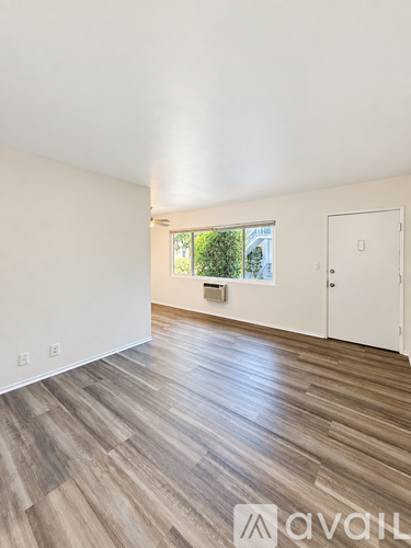 A room with wooden flooring and a window showing greenery outside.