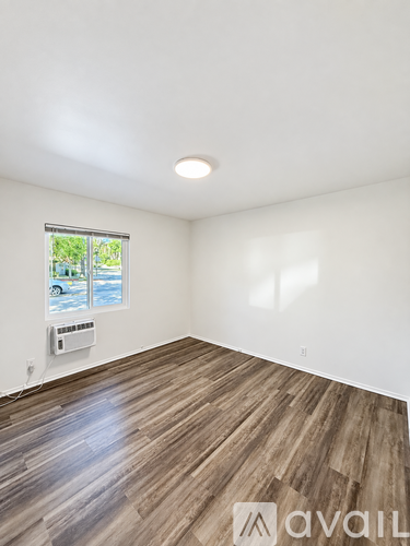 A room with wooden flooring and a window showing a parking lot outside.