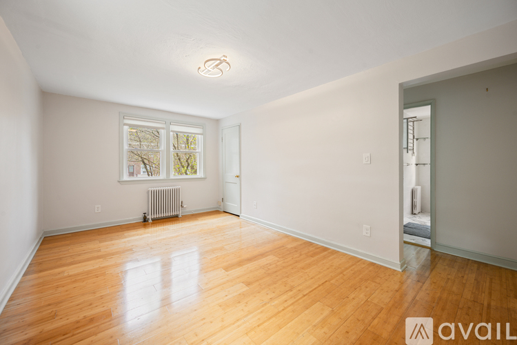 A room with wooden floors and a window with a view of trees and a radiator on the floor.