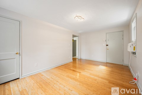 A room with wooden floors and white walls, with a door on the left and a window on the right.