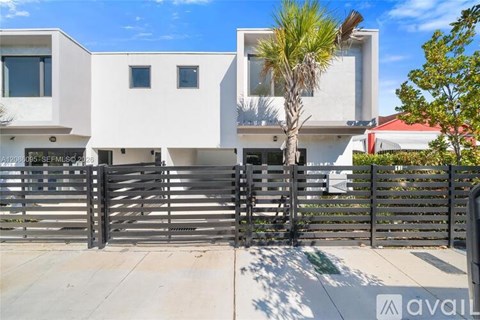 A modern white house with a black gate and a palm tree in front.