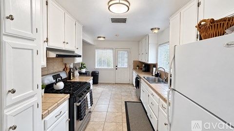 A kitchen with white cabinets and appliances, a black stove, and a window with blinds.