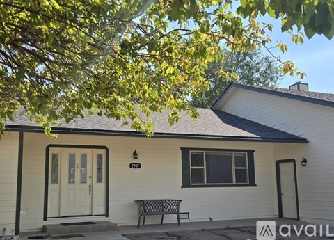 A house with a white exterior and a black roof has a bench in front of it.