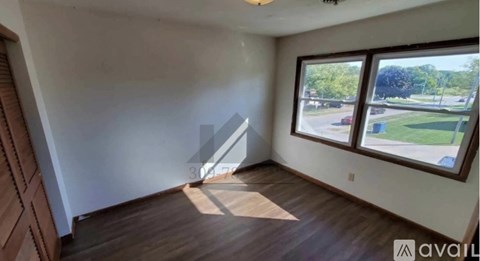 A room with wooden floors and a large window overlooking a parking lot.