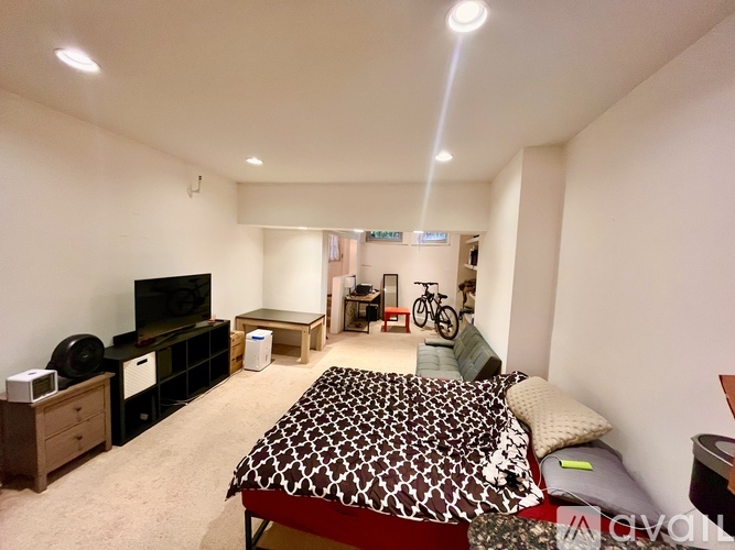 A bedroom with a bed, a TV, a bicycle, and a trash can.