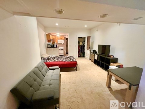A living room with a grey couch and a red bedspread.