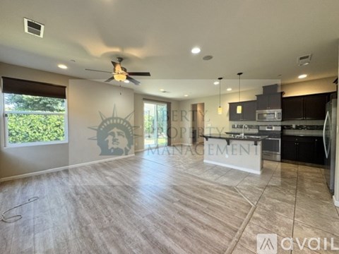 A spacious room with a ceiling fan and a kitchen area in the background.