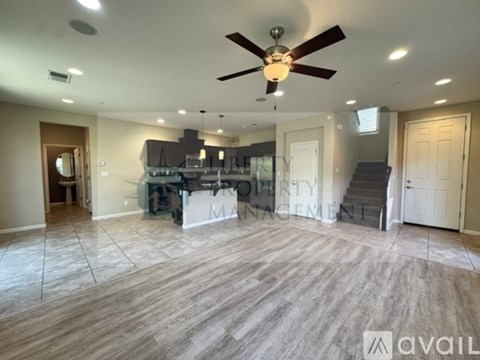 A spacious room with a ceiling fan and a kitchen area in the background.