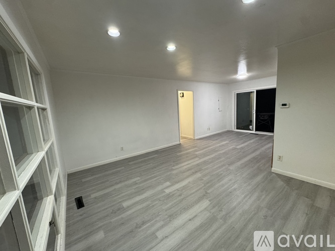 A room with wooden flooring and white walls, with a door in the middle of the room.