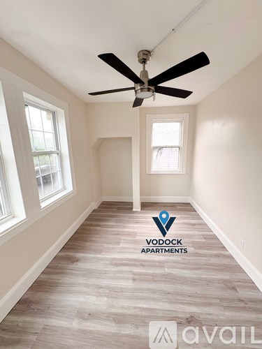 A room with a ceiling fan and Vodock Apartments logo on the floor.