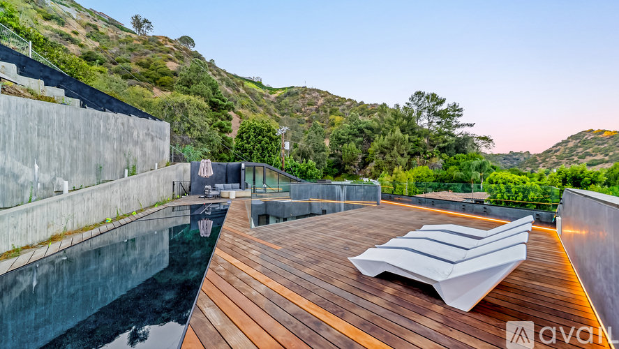 A wooden deck with a sun lounger and a pool in the foreground with a hill in the background.