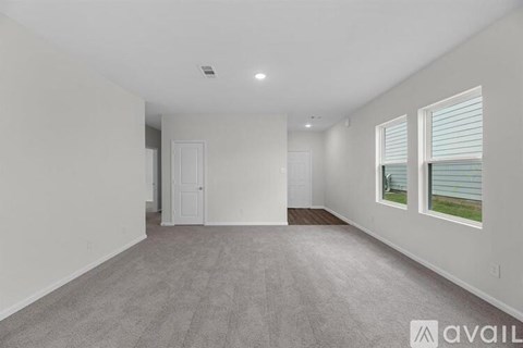 A spacious room with a carpeted floor and two windows.