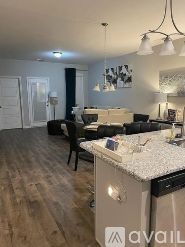 A kitchen with a granite countertop and a dining area with a black chair and a white sofa.