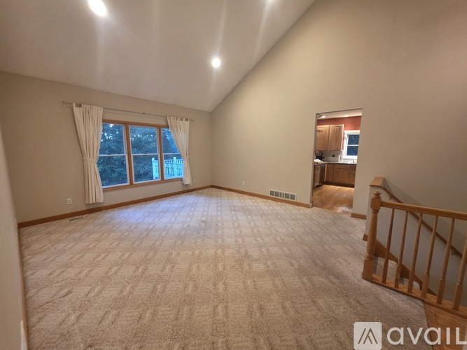 A spacious room with a carpeted floor and a window with curtains.