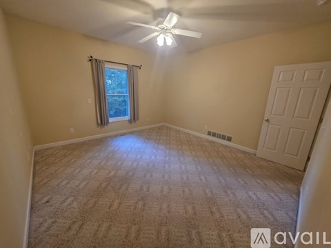 A room with a carpeted floor, a ceiling fan, and a window with a view of trees outside.