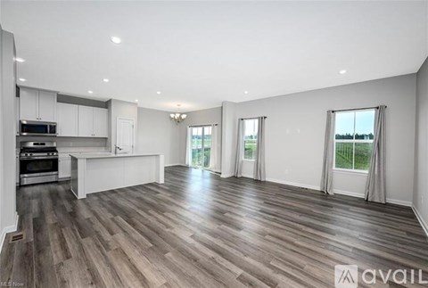 A spacious living room with hardwood floors and a kitchen area in the background.