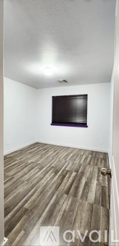 A room with wooden flooring and a window with blinds.