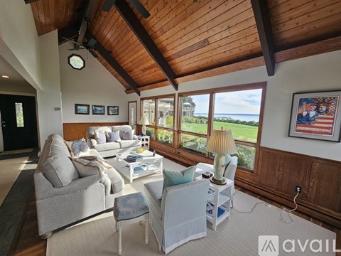 A living room with a grey couch, a white chair, and a wooden ceiling.