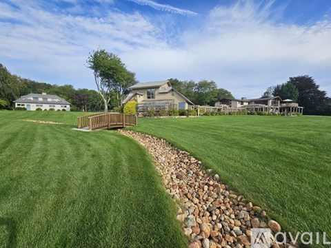A large grassy field with a stone path leading to a wooden fence and a house in the distance.