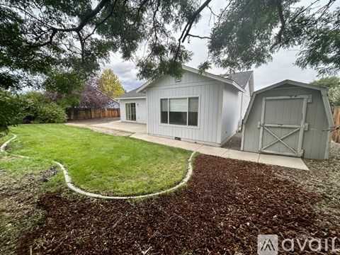 A house with a grey exterior and a grey garage door is surrounded by a garden with a white curved path.