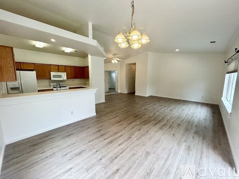 A spacious living room with wooden flooring and a kitchen area in the background.