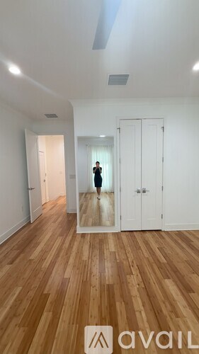 A person stands in a room with wooden floors and white walls.