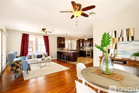 A living room with a white ceiling fan and a dining table with a vase of flowers on it.